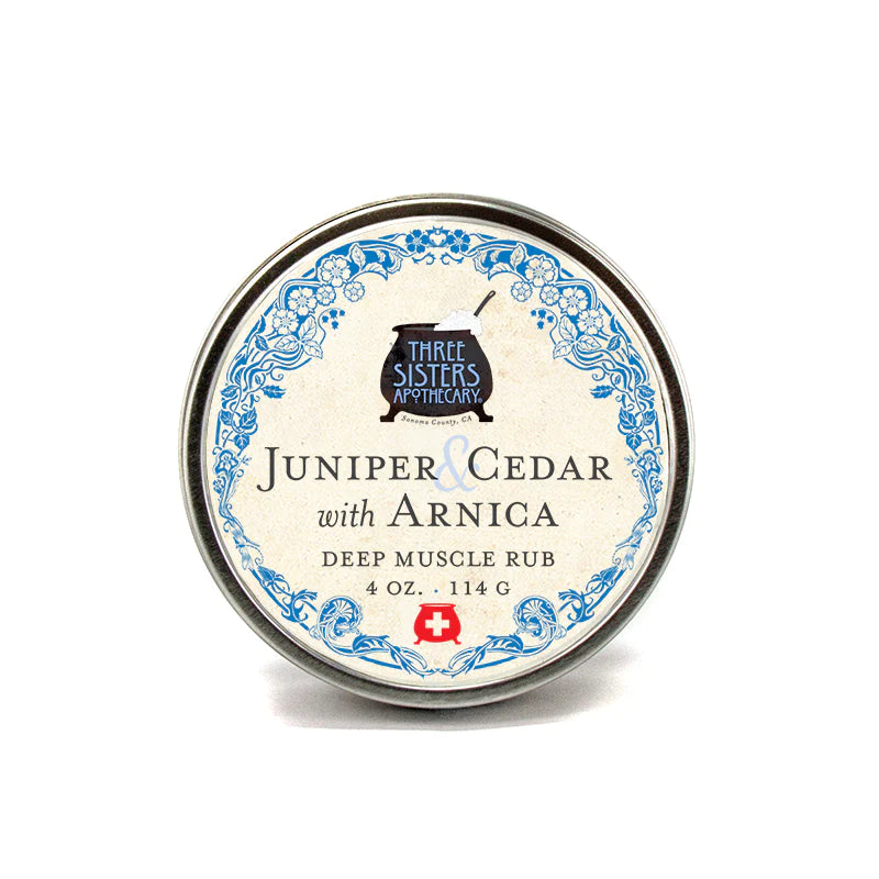 A round tin of Three Sisters Aphothecary Juniper Cedar & Arnica Muscle Rub, featuring an ornate blue and white label, isolated on a white background.