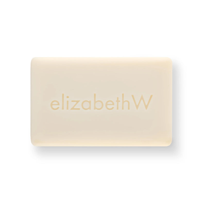 A rectangular, cream-colored bar of soap with "elizabethW" embossed on its surface. Made with plant-based ingredients and a hint of cucumber essence, the elizabeth W Purely Essential Cucumber Triple-Milled Soap is set against a white backdrop, making it the focal point of the image.