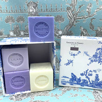 An array of Senteurs De France Coffret Lavender, Violet, Lilac, Jasmine Cube Soaps with labels violette, lilas, lavande, and jasmin, displayed in front of a box with traditional blue toile de jouy pattern.