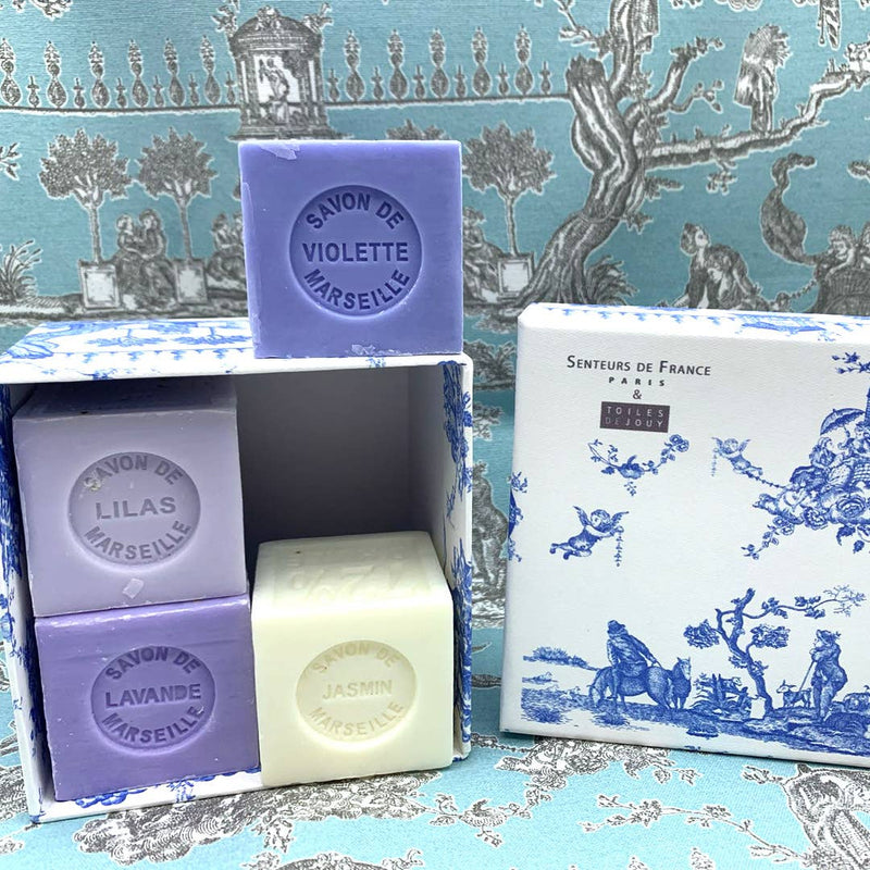 An array of Senteurs De France Coffret Lavender, Violet, Lilac, Jasmine Cube Soaps with labels violette, lilas, lavande, and jasmin, displayed in front of a box with traditional blue toile de jouy pattern.