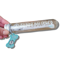 A hand holds a transparent tube labeled "Wag & Bright Supply Co. - Puppy Polisher Mini Eco Toothbrush (Small)," highlighting its eco-friendly toothbrush made from sustainable bioplastic for dogs. The cap is decorated with a blue, bone-shaped tag, and it features 5000 silky PBT bristles to ensure gentle care for your pet.