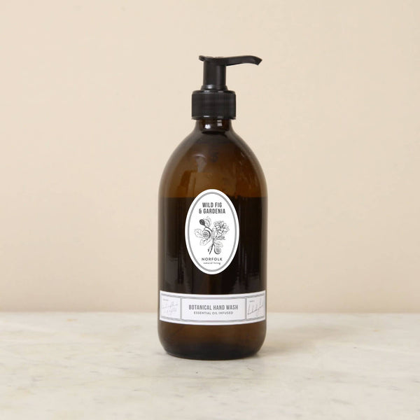 A 500ml brown glass pump bottle of Norfolk Natural Living Wild Fig & Gardenia Gardener's Hand Wash sits on a white surface against a beige background.