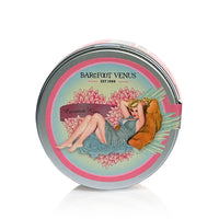 A round tin container of Barefoot Venus Coconut Kiss Sugar Body Scrub. The paraben-free sulfate-free tin features vintage-style artwork of a reclining woman in a blue dress against a pink floral background. The product name and brand are printed on the lid.