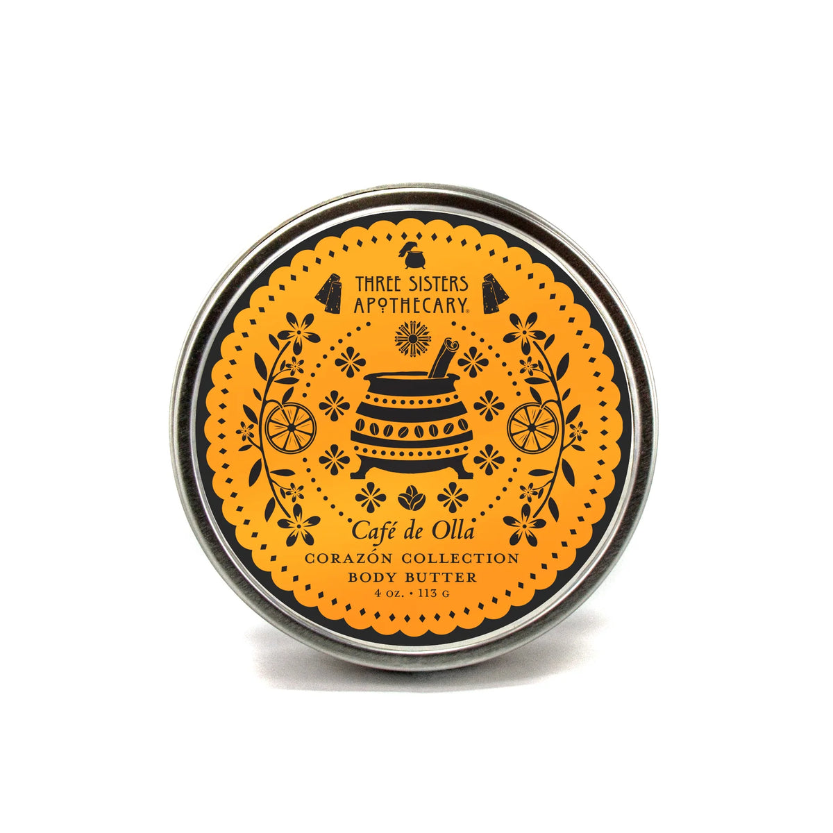 A round tin of Three Sisters Apothecary Café de Olla Body Butter - Corazón Collection features a decorative orange label with black teapot, flower, and citrus illustrations, emphasizing plant-based hydration.