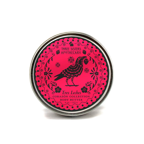 A 4 oz (113 g) round tin of Three Sisters Apothecary Tres Leches Body Butter – Corazón Collection features a black bird and floral design on bright pink. This natural product is from Three Sisters Aphothecary.