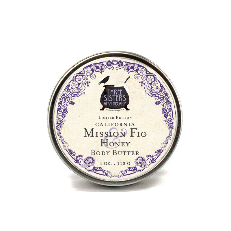 A round tin with a label for "Three Sisters Apothecary Mission Fig & Honey Body Butter, 4 oz., 113g" in vintage style with ornate purple designs around the edges.
