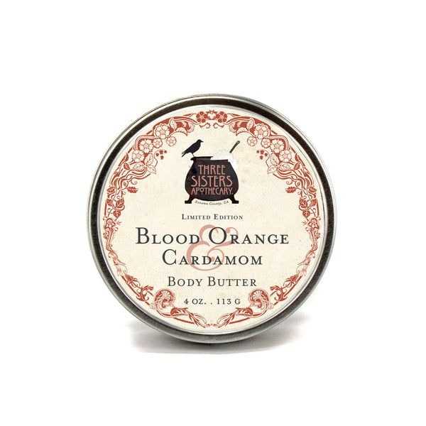 A 4 oz (113 g) tin of Three Sisters Apothecary Blood Orange & Cardamom Body Butter, featuring ornate red floral designs and black lettering on a white label; this is a limited edition from Three Sisters Apothecary.