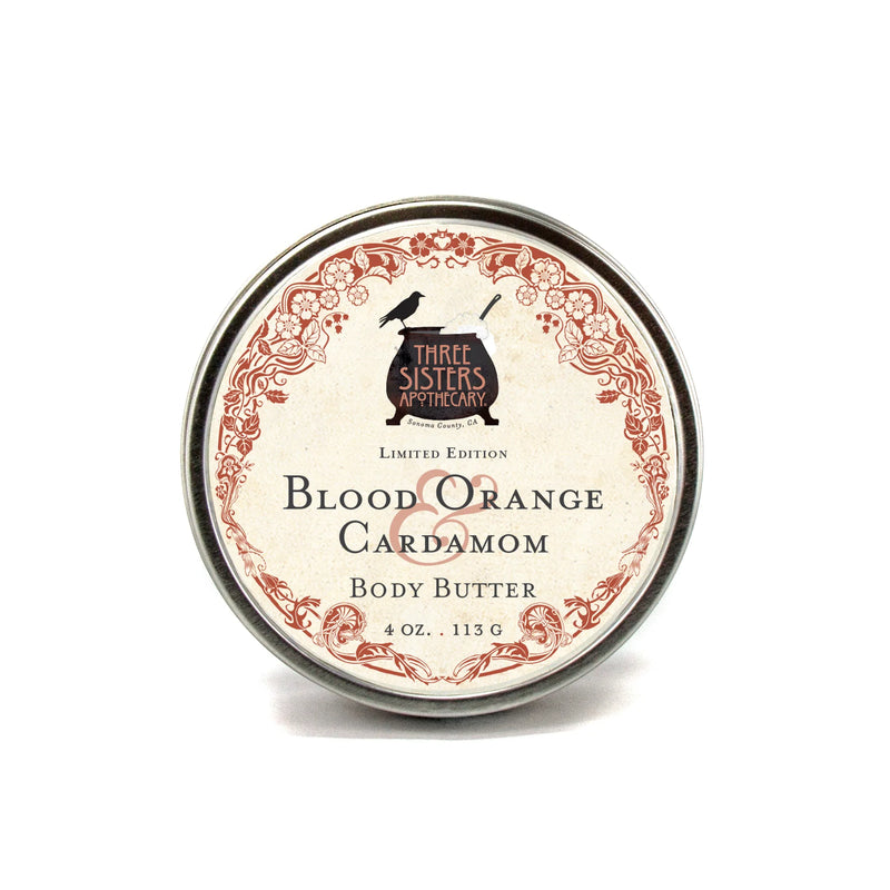 A 4 oz (113 g) tin of Three Sisters Apothecary Blood Orange & Cardamom Body Butter, featuring ornate red floral designs and black lettering on a white label; this is a limited edition from Three Sisters Apothecary.