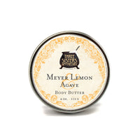 A round tin of Three Sisters Apothecary Meyer Lemon & Agave Body Butter, 4 oz (113 g), features a decorative yellow floral border and offers a fresh scent with rich, natural hydration.