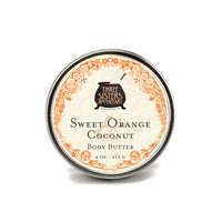 A 4 oz. tin of Three Sisters Apothecary Sweet Orange & Coconut Body Butter, featuring an ornate orange border and black text on cream, with nourishing coconut oil and shea butter.