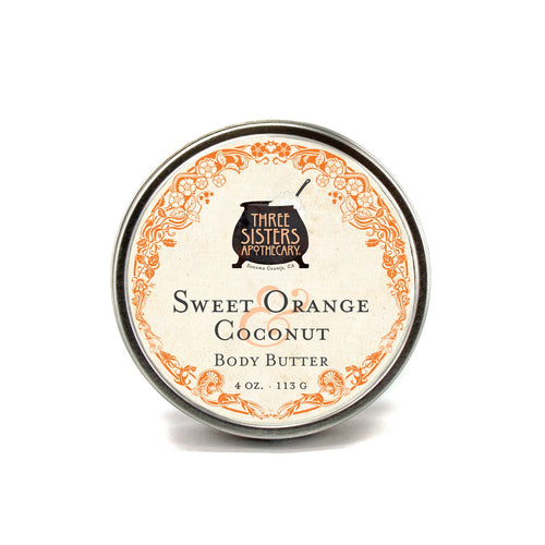 A 4 oz. tin of Three Sisters Apothecary Sweet Orange & Coconut Body Butter, featuring an ornate orange border and black text on cream, with nourishing coconut oil and shea butter.