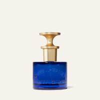 A blue glass Caswell Massey Elixir of Love Eau de Toilette bottle with “CASWELL-MASSEY PERFUMERS” embossed and a gold sculptural spray cap holds this cruelty-free floral fragrance, shown against a plain light background.