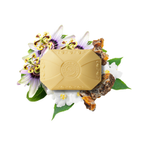 A Caswell-Massey Elixir of Love Three-Soap Set by Caswell Massey is surrounded by white and purple passionflowers, amber resin pieces, and green leaves on a white background.