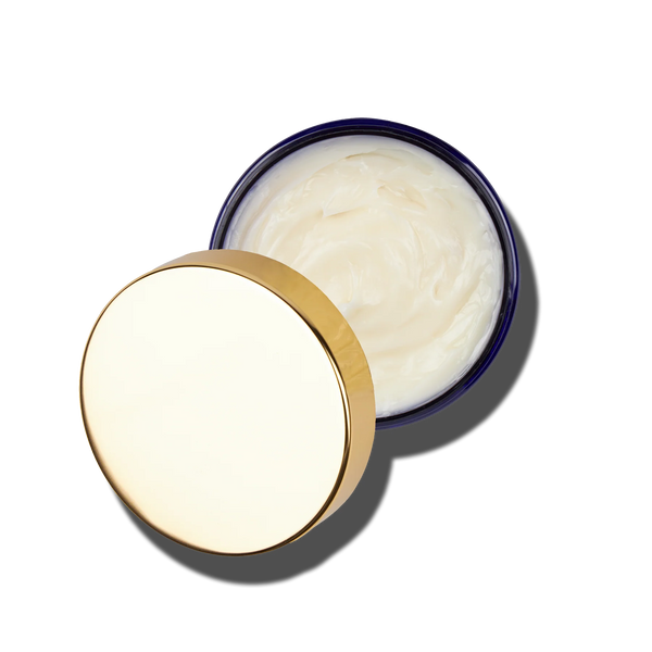 An open Caswell-Massey Elixir of Love Body Cream jar in dark blue with a shiny gold lid to the side, revealing the creamy white moisturizing formula inside, is shown on a light background.