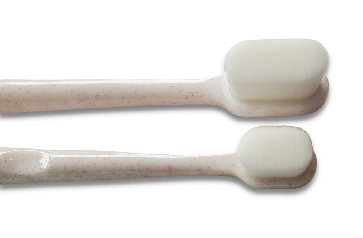 Two Wag & Bright Supply Co. Puppy Polisher Mini Eco Toothbrushes (Small), designed with sustainable bioplastic, showcase smooth white bristles and lightly speckled handles. Their minimalist aesthetic harmonizes with the eco-friendly materials against a white background.