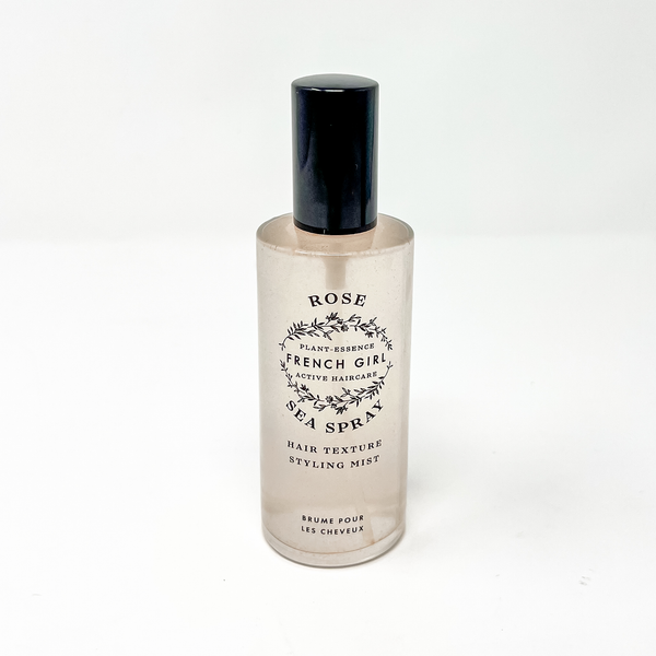 A clear bottle of FRENCH GIRL Organic Sea Salt Hair Mist & Texturizing Spray - Rose features a black cap and label with black botanical designs on white, perfect as a sea salt mist for beachy waves.