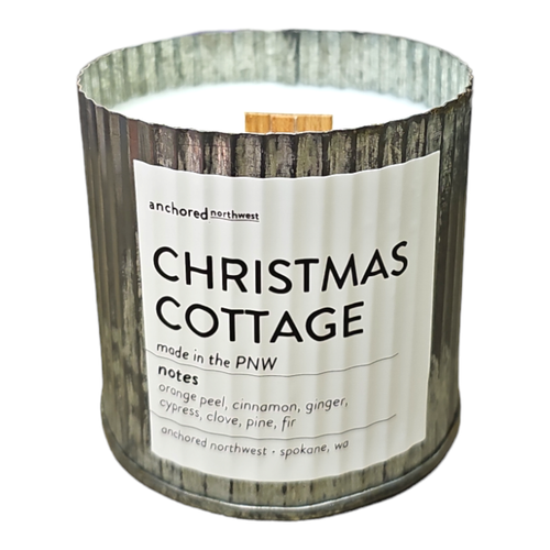 The Anchored Northwest Christmas Cottage Rustic Vintage Farmhouse Wood Wick Candle is a decorative piece with a metal exterior and a wood wick. It imbues your space with an aroma of orange peel, cinnamon, ginger, clove, cypress, pine, and fir. This candle is crafted in Spokane, WA.