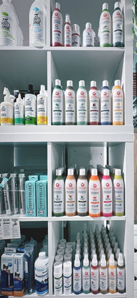 Shelves filled with various bottles of cleaning and hygiene products, including sprays and liquids, organized neatly. Among them are items like the Puppy Polisher Eco Toothbrush (Medium), expertly crafted by Wag & Bright Supply Co. Some of these products are made from sustainable wheat straw bioplastic. Labels in different colors indicate diverse solutions designed to efficiently address your hygiene needs.