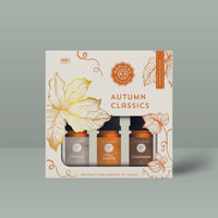 The Woolzies Autumn Classics Collection is a boxed set of three fall-inspired essential oils—Vanilla, Fall Nights, and Cinnamon—packaged with orange floral and leaf designs and "Autumn Classics" text on a beige and orange background.