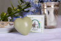 The Senteurs De France Olive Heart Soap - Marquise and Her Dog, shaped like a heart, sits before its decorative "Senteurs De France" box, with blue flowers and a silver container in the background on a white cloth.