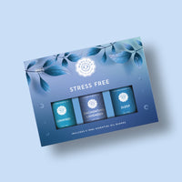 A blue gift box labeled "Woolzies Stress Free Collection" by Woolzies contains three 10ml calming oils: Unwind, Enchanting Lavender, and Sleep. The packaging displays leaf illustrations and a soothing gradient background.