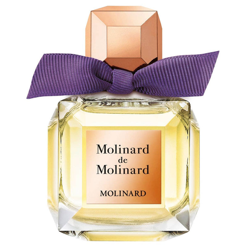 A square glass bottle labeled "Molinard de Molinard" by Molinard features a gold cap, purple bow, and contains pale yellow Eau de Toilette with floral and woody oriental notes.