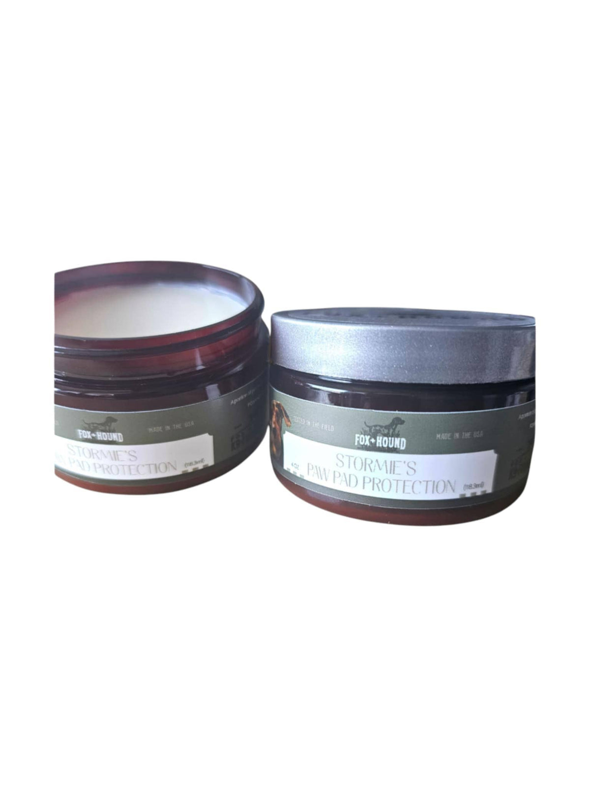 Two containers of Fox + Hound Stormies Paw Protection - All Season, an all-natural balm for dog paw care—one open to show the cream, one closed with a gray lid—are displayed against a white background.