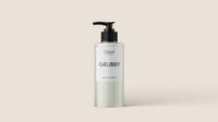 A sleek, transparent bottle with a black pump top, filled with a light green liquid labeled "GRUBBY" at the center. The white label features the brand name "L'floof" on top and "Natural Dog Shampoo" at the bottom. Enhanced with Peppermint/Eucalyptus. The background is plain and beige.