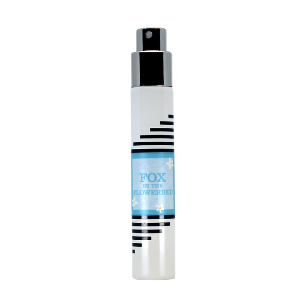 A sleek, travel-sized cylindrical perfume bottle with a polished silver nozzle and cap. The bottle showcases bold black horizontal stripes and a blue label displaying the text "Imaginary Authors Fox in the Flowerbed." Channeling ethereal elegance, this floral fragrance interweaves notes of Jasmine Tulips, all set against a plain white background.