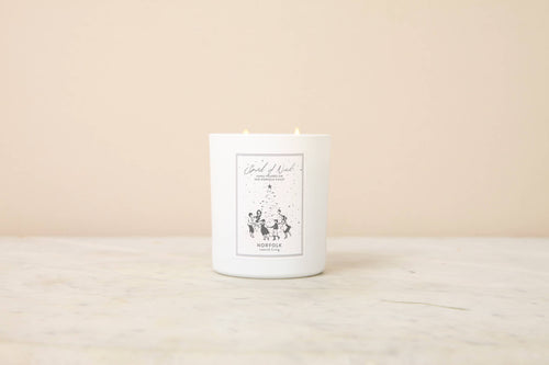 A white soy wax candle from Norfolk Natural Living rests on marble, its minimalist label reading “Spirit of Noel Christmas Candle”—the perfect cozy touch for winter evenings.