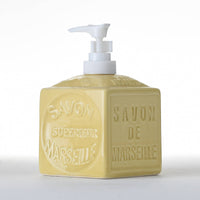 The "French Soaps Liquid Soap Dispenser Savon de Marseille" by FRENCH SOAPS is a traditional yellow ceramic soap dispenser featuring a white pump. The sides of the cube are embossed with the text "SAVON SUPERIEUR MARSEILLE" and "SAVON DE MARSEILLE," sitting on a plain white background that evokes the classic charm of authentic Savon de Marseille.