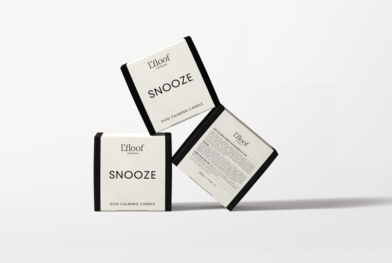 Three white and black L'floof SNOOZE Dog Calming Candle boxes are displayed: two show the product name, while the third highlights the essential oil formula on the back, designed to promote pet relaxation. Each candle contains 330ml.