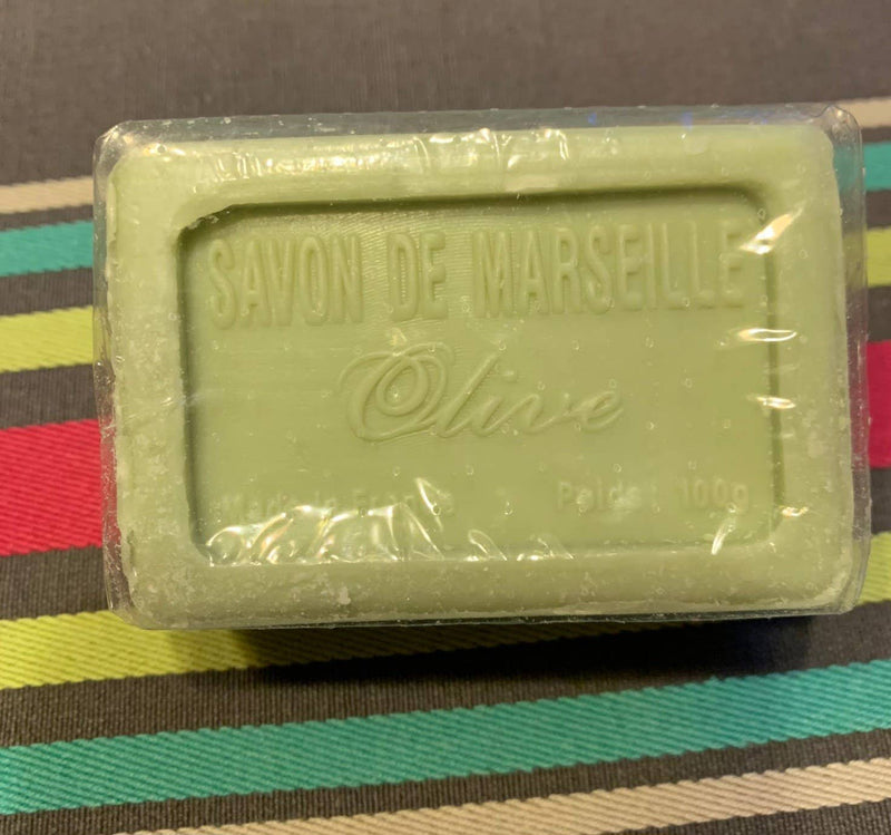A green rectangular Senteurs De France Olive Oil Marseille Soap bar, with raised lettering and clear plastic wrap, sits on a colorful striped surface.