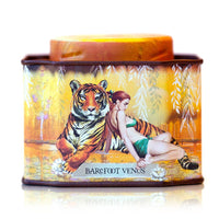 A decorative tin for Barefoot Venus Apricot Brandy Bath Soak features a woman in a green dress beside a tiger on a golden background with white leaves, combining handcrafted luxury with indulgent apricot scent.