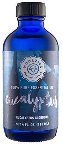 A blue glass bottle labeled "Woolzies Eucalyptus Essential Oil" by Woolzies stands against a plain background, highlighting the brand and its natural cleaning benefits.
