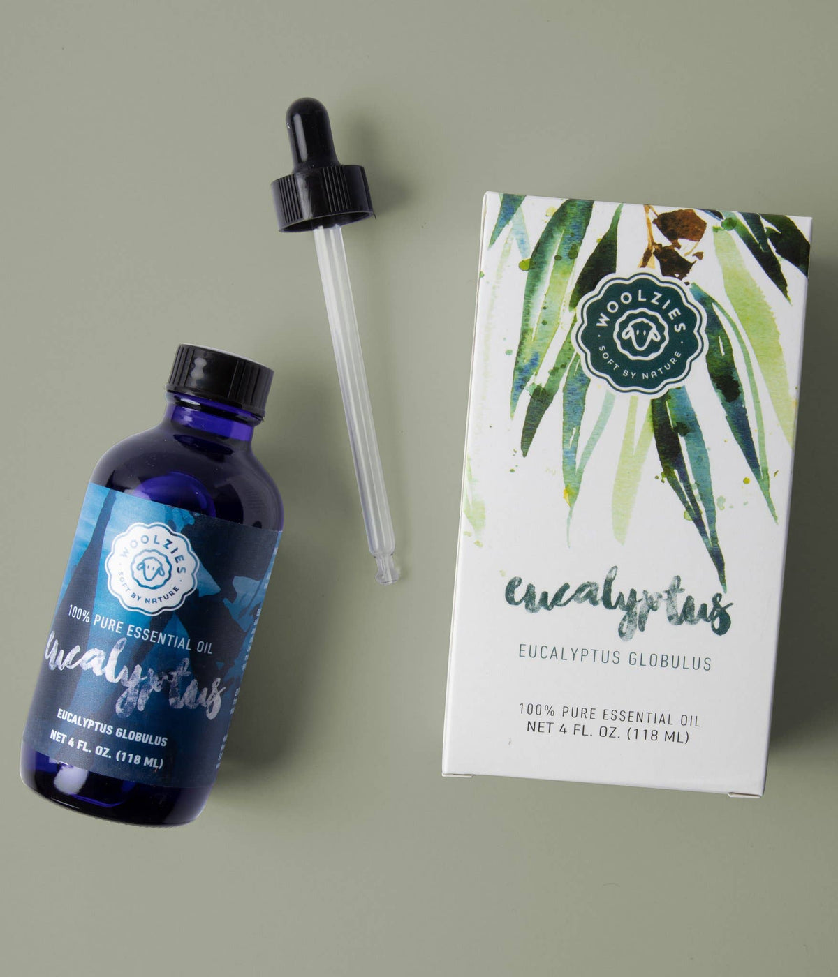 A bottle of Woolzies Eucalyptus Essential Oil with a dropper and its illustrated box on a green surface—a natural cleaner by Woolzies that also helps support respiratory health.