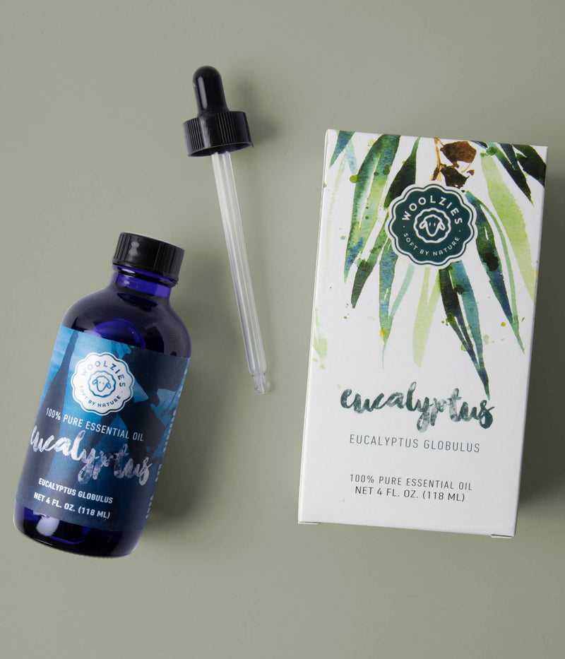 A bottle of Woolzies Eucalyptus Essential Oil with a dropper and its illustrated box on a green surface—a natural cleaner by Woolzies that also helps support respiratory health.