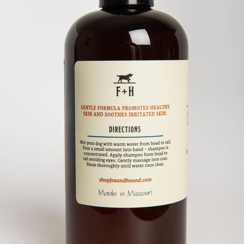 Close-up view of a brown Fox + Hound 2-in-1 shampoo and conditioner bottle with a beige label displaying text, a logo, and usage instructions, against a plain background. The label reads "f+h" and "made in Missouri".