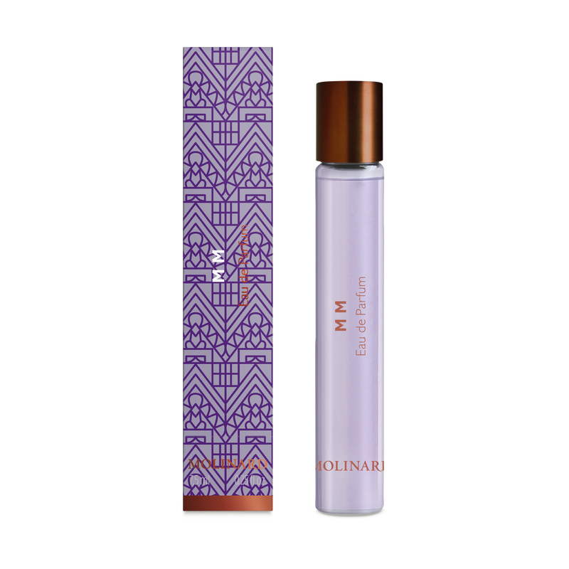 A slim glass roll-on bottle labeled "Molinard MM Eau de Parfum" with a copper cap stands beside a purple, art deco-patterned box with copper accents, suggesting an elegant woody scent. The background is white.