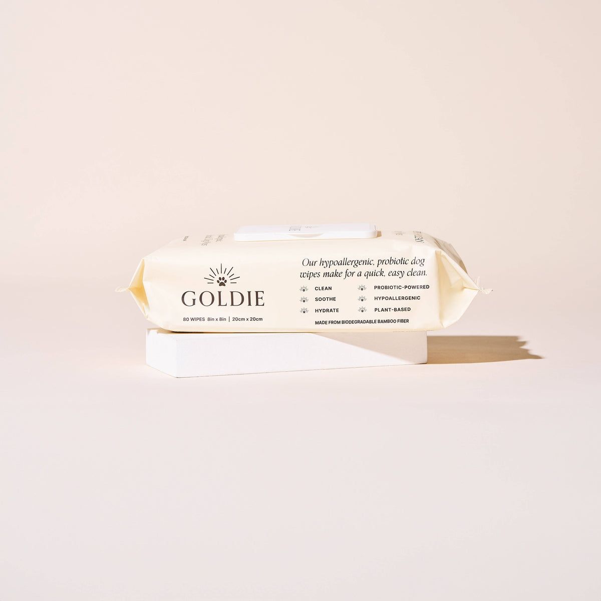 A package of Goldie - So Fresh, So Clean Probiotic Wipes for dogs rests on a white rectangular block with a beige background. The packaging features plant-based, hypoallergenic, soothing, hydrating, and biodegradable benefits.
