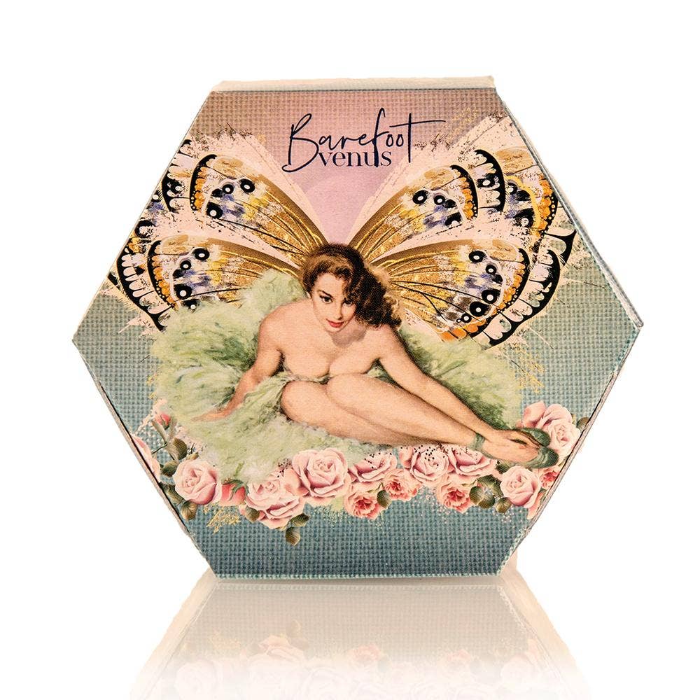 Hexagonal box adorned with a vintage-style illustration of a seated woman with butterfly wings, encircled by pink roses. "Barefoot Venus," the brand behind The Vanilla Effect Bath Bliss Soak, is prominently displayed at the top, suggesting its all-natural ingredients. The whimsical design is further enhanced by a soft teal background that embodies purity and grace.