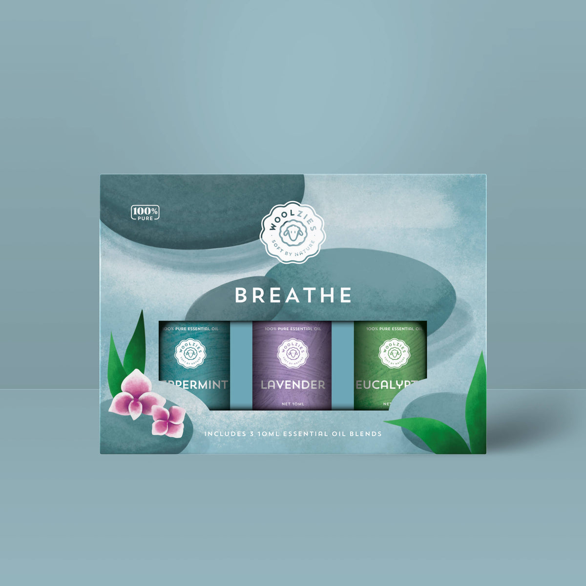 Woolzies The Breathe Essential Oil Collection by Woolzies includes three blends—peppermint, lavender, and eucalyptus—in a box adorned with green leaves, pink flowers, and a soft blue background for a calming look.