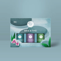 Woolzies The Breathe Essential Oil Collection by Woolzies includes three blends—peppermint, lavender, and eucalyptus—in a box adorned with green leaves, pink flowers, and a soft blue background for a calming look.