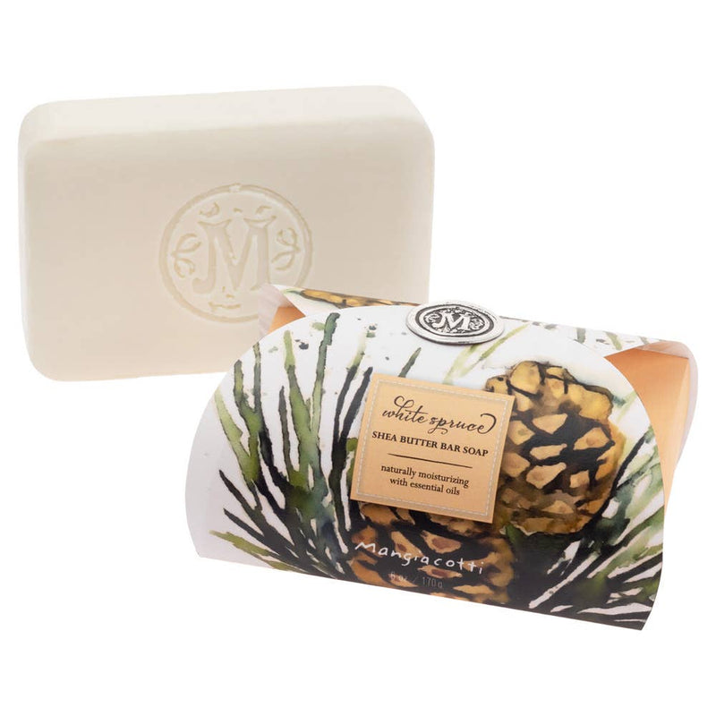 A bar of Mangiacotti White Spruce Shea Butter Bar Guest Soap 6 oz, featuring a pure white rectangular form with an embossed logo. The soap packaging is decorated with botanicals and a central label detailing natural moisturizing with essential oils. This natural biodegradable soap ensures gentle care for your skin and the environment.