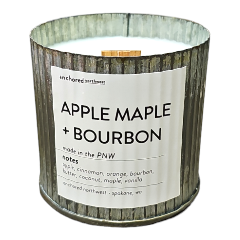 The Anchored Northwest Apples & Maple Bourbon Rustic Vintage Farmhouse Wood Wick Candle is housed in a glass container and features a label that reads “Anchored Northwest - Apple Maple + Bourbon - made in the PNW.” This soy wax candle, made in Spokane, WA, exudes notes of apple, cinnamon, orange, bourbon, butter, coconut, maple, and vanilla.