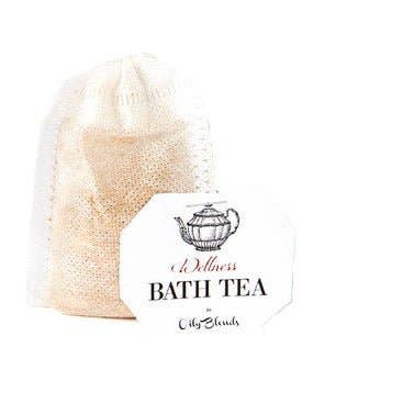 Beside an ornate label featuring a teapot, a mesh bag of bath tea promises relaxation and moisturizing benefits. The label reads "Bath Tea Single Bag - Wellness" by Hampton Court, maintaining a clean and minimalistic tone.