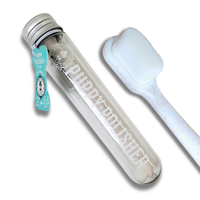 A transparent tube labeled "Wag & Bright Supply Co. - Puppy Polisher Eco Toothbrush - (Medium)" with a silver cap and a turquoise tag, highlighting pet dental health benefits, is positioned beside a white brush made from wheat straw bioplastic. The tag includes text and a small logo design. Both items are set against a simple white background.