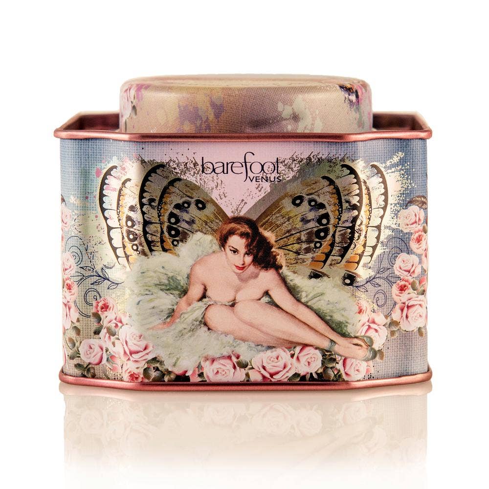 A decorative tin featuring a vintage-style illustration of a woman with butterfly wings amidst roses, labeled "Barefoot Venus The Vanilla Effect Bath Soak." The soft pink and gold tin contains a cruelty-free vanilla bath soak made from plant-based ingredients for an indulgent experience.