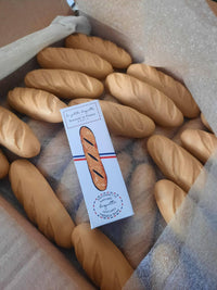 Senteurs De France "Baguette" Soap features realistic baguette-shaped soaps arranged in a box, centered around a small illustrated box with French text—creating a playful bakery-inspired keepsake.
