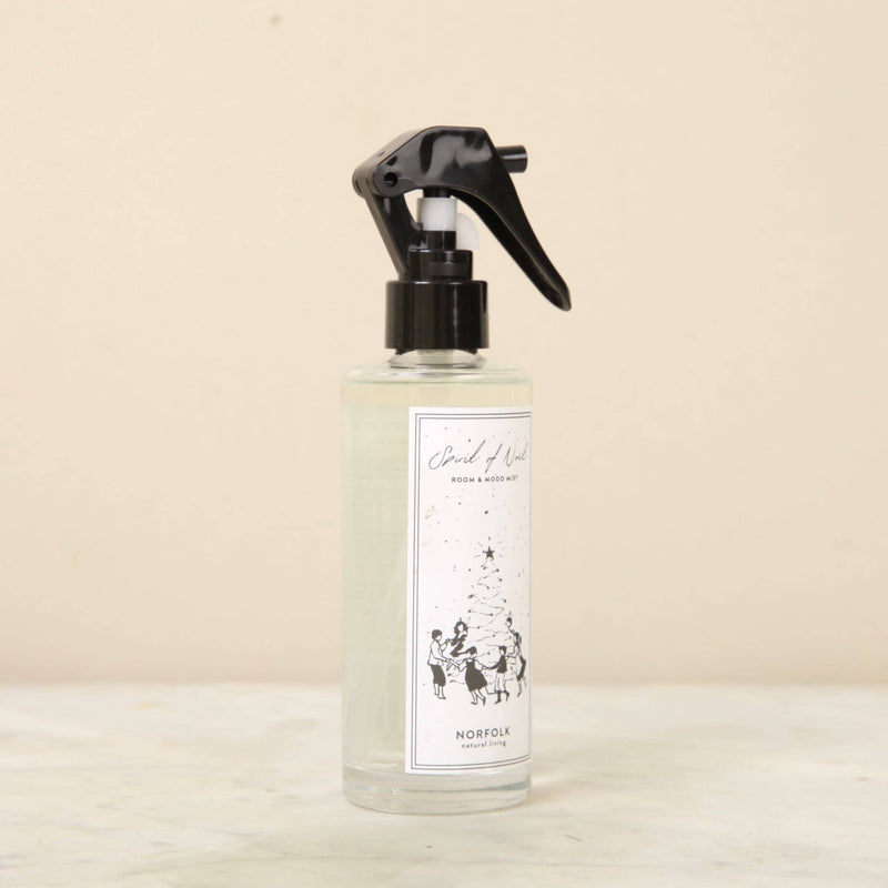 A clear spray bottle with a black trigger nozzle sits on a light surface. The label reads "Norfolk Natural Living Spirit of Noel Christmas Room Mist," ideal for adding festive fragrance and a cozy ambiance to any space.